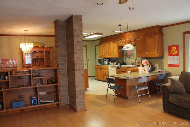 kitchen featuring light wood-style floors, brown cabinets, crown molding, and decorative columns