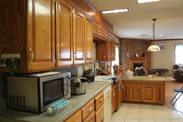 kitchen featuring white dishwasher, a peninsula, a brick fireplace, brown cabinets, and stainless steel microwave