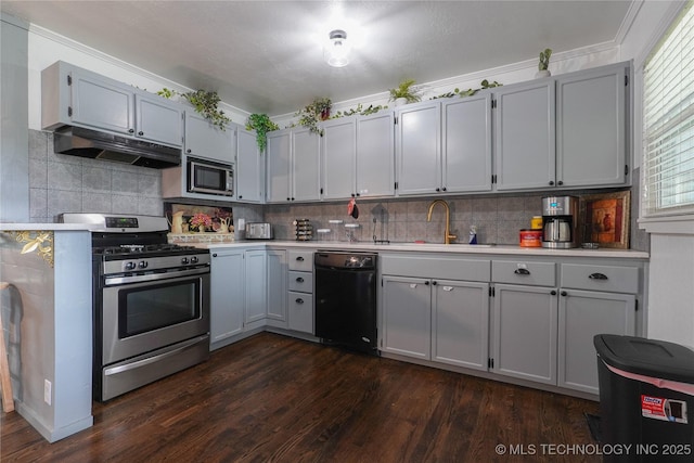 kitchen featuring dark wood finished floors, stainless steel appliances, light countertops, under cabinet range hood, and a sink