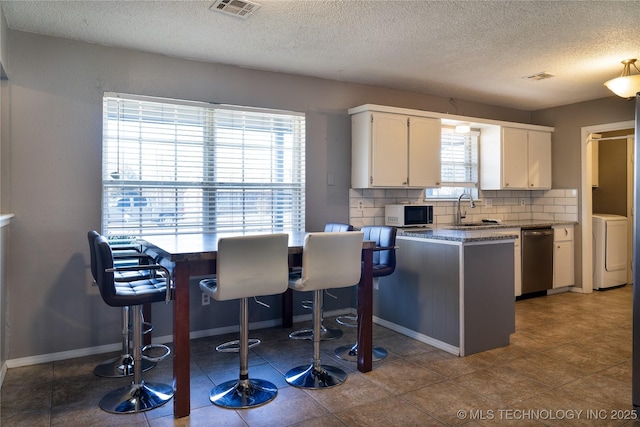 kitchen featuring tasteful backsplash, washer / clothes dryer, white cabinets, a sink, and dishwasher