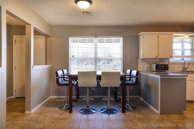 dining space with visible vents, a textured ceiling, baseboards, and tile patterned floors