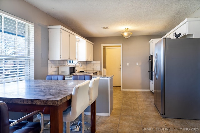 kitchen featuring stainless steel refrigerator with ice dispenser, light tile patterned floors, backsplash, white cabinets, and a sink