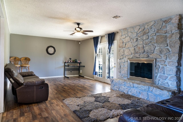 unfurnished living room with a stone fireplace, wood finished floors, visible vents, baseboards, and a ceiling fan