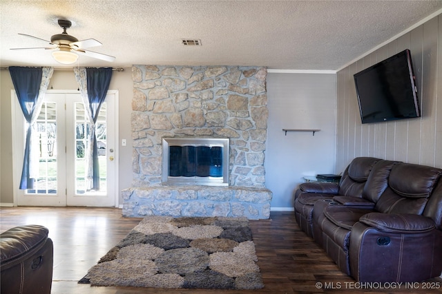 living room with a textured ceiling, visible vents, wood finished floors, and a stone fireplace