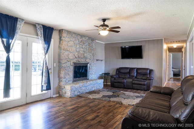 living area with ceiling fan, a stone fireplace, plenty of natural light, and wood finished floors