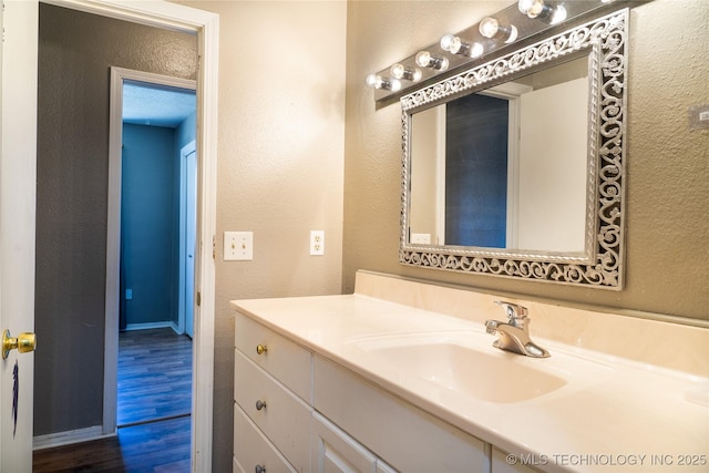 bathroom featuring vanity, baseboards, wood finished floors, and a textured wall