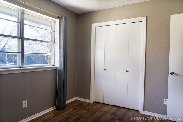 unfurnished bedroom with baseboards, dark wood finished floors, a textured wall, a textured ceiling, and a closet