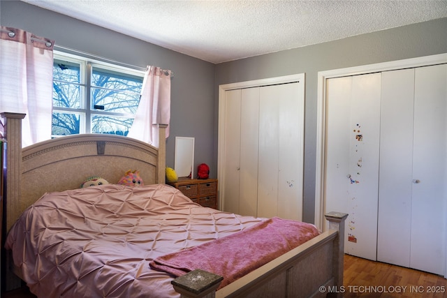 bedroom featuring multiple closets, a textured ceiling, and wood finished floors