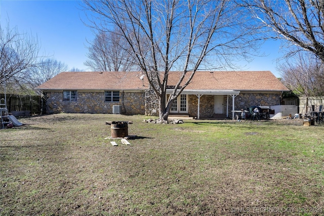 rear view of property featuring stone siding, a lawn, and fence