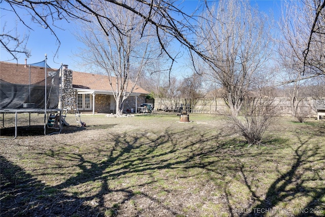 view of yard featuring a trampoline, french doors, and fence