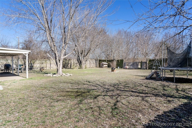 view of yard featuring a trampoline, fence, a playground, and a patio