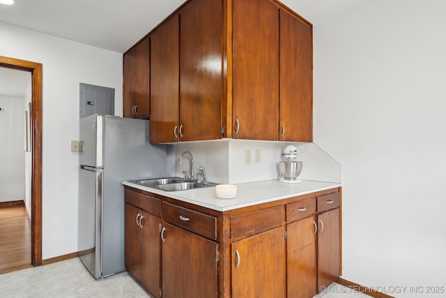 kitchen with electric panel, freestanding refrigerator, a sink, light countertops, and backsplash