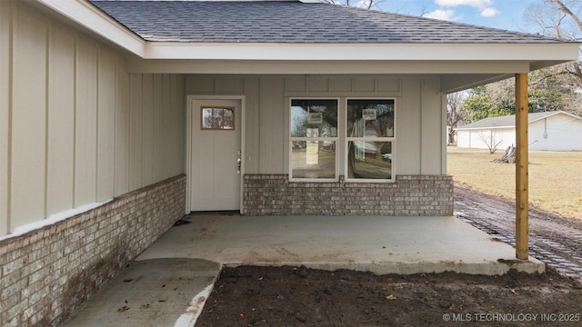 doorway to property featuring roof with shingles, a patio, and brick siding