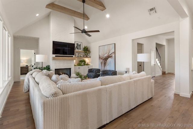 living area featuring visible vents, hardwood / wood-style floors, beamed ceiling, a fireplace, and high vaulted ceiling