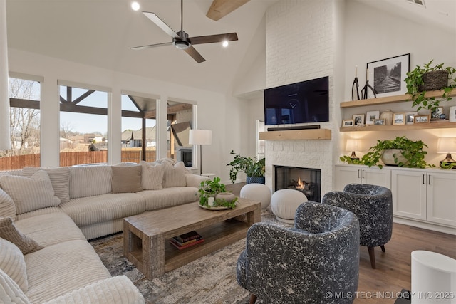 living area with high vaulted ceiling, a fireplace, wood finished floors, a ceiling fan, and beam ceiling