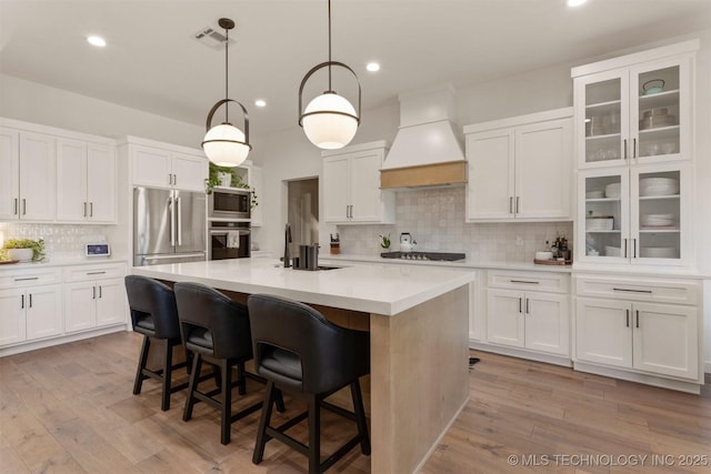 kitchen featuring stainless steel appliances, light wood-style floors, white cabinetry, a sink, and premium range hood