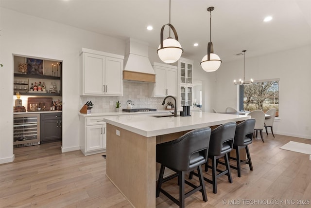 kitchen with beverage cooler, premium range hood, a sink, and light wood-style flooring