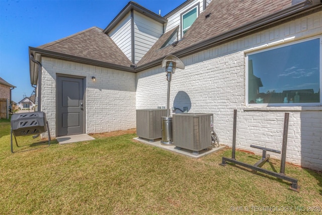 back of property featuring central AC unit, a lawn, and a shingled roof