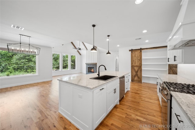 kitchen featuring a barn door, a fireplace, a sink, appliances with stainless steel finishes, and custom range hood