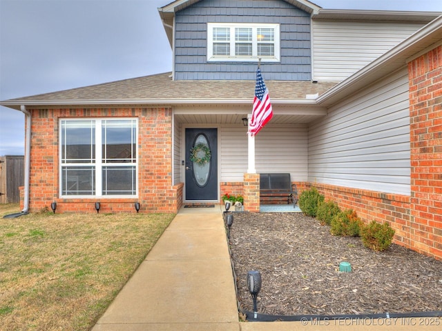 entrance to property featuring a shingled roof, brick siding, and a yard