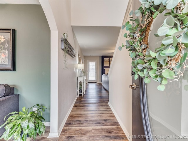 corridor with arched walkways, baseboards, and wood finished floors