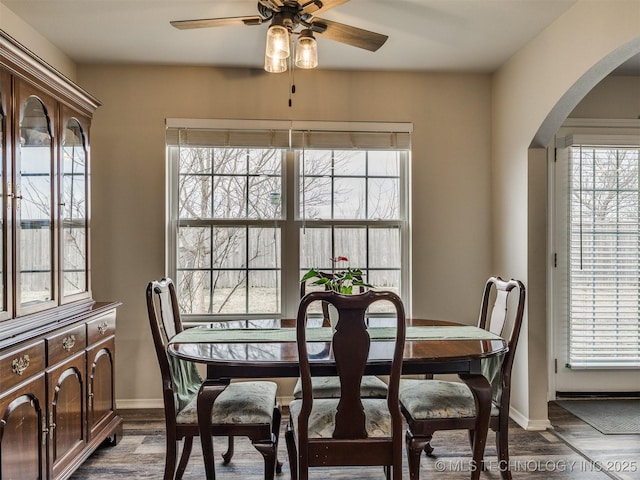 dining space with arched walkways, dark wood finished floors, baseboards, and ceiling fan