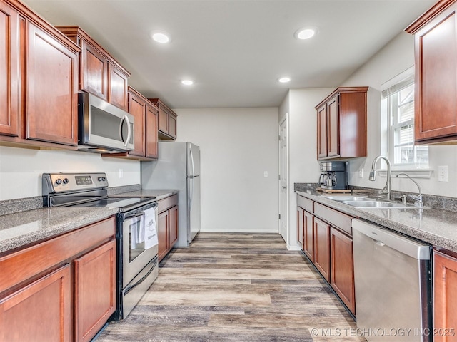 kitchen with light wood finished floors, stone countertops, stainless steel appliances, a sink, and recessed lighting