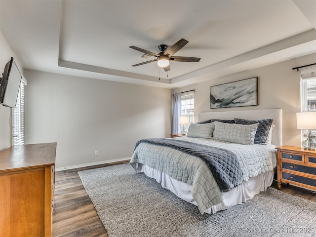 bedroom featuring dark wood-style floors, a raised ceiling, a ceiling fan, and baseboards