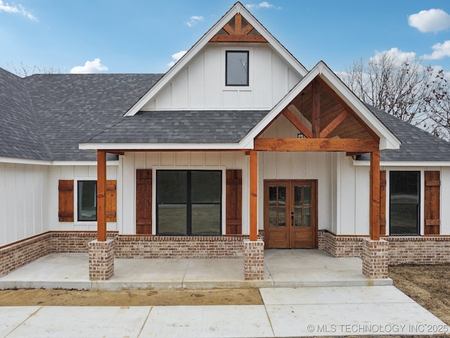 doorway to property with brick siding, a shingled roof, board and batten siding, and french doors