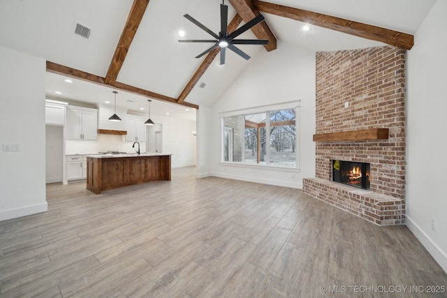 unfurnished living room with high vaulted ceiling, a fireplace, a ceiling fan, light wood-type flooring, and beamed ceiling