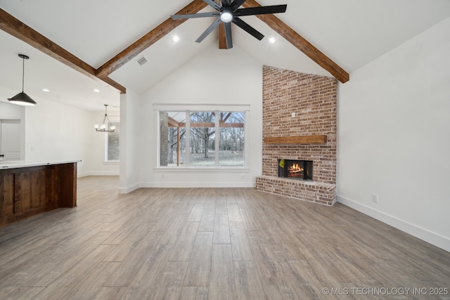 unfurnished living room with light wood-style flooring, beamed ceiling, a fireplace, high vaulted ceiling, and ceiling fan with notable chandelier