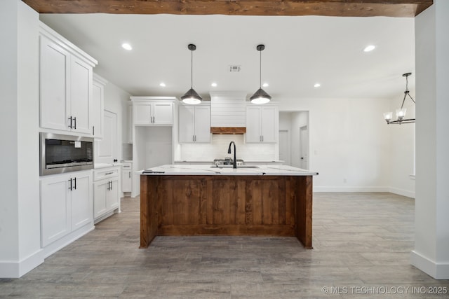 kitchen featuring visible vents, decorative backsplash, white cabinets, built in microwave, and a sink