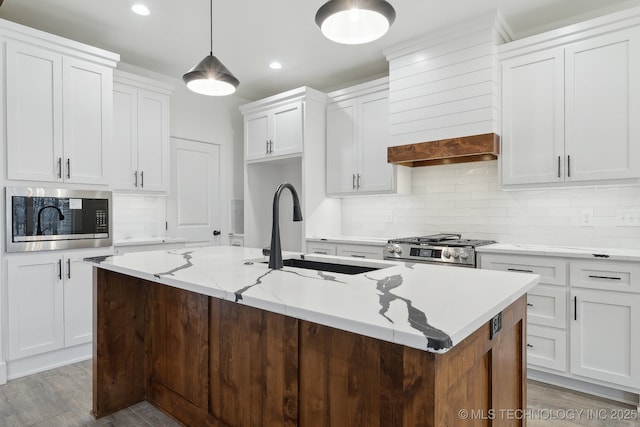 kitchen featuring white cabinets, wall chimney range hood, stainless steel appliances, and a sink