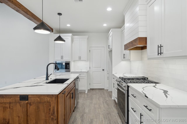 kitchen with white cabinets, appliances with stainless steel finishes, a kitchen island with sink, light wood-style floors, and a sink