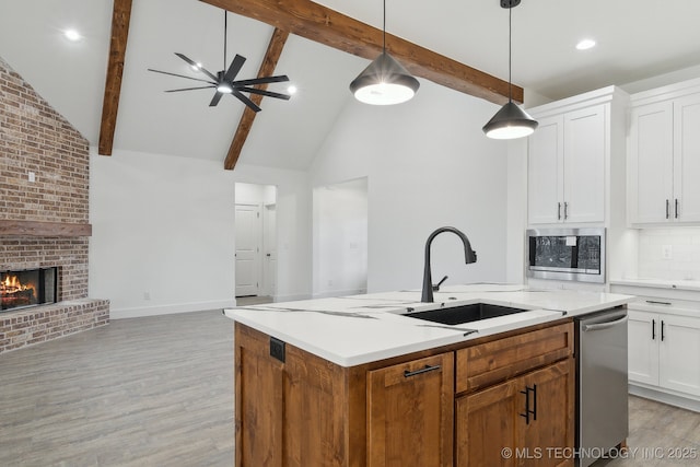 kitchen featuring appliances with stainless steel finishes, open floor plan, a brick fireplace, white cabinetry, and a sink