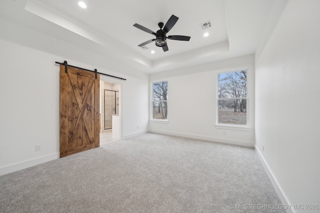 unfurnished bedroom featuring light colored carpet, a tray ceiling, visible vents, and a barn door