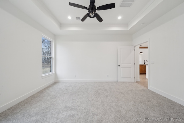 empty room featuring light colored carpet, a raised ceiling, visible vents, and baseboards