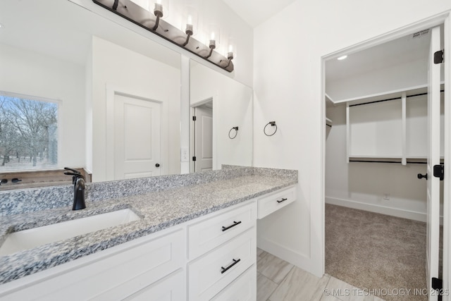 bathroom featuring visible vents, a walk in closet, vanity, and baseboards