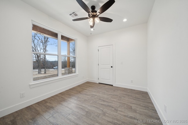 empty room featuring a ceiling fan, visible vents, baseboards, and wood finished floors