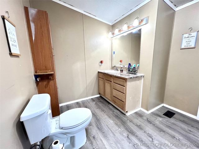 bathroom with crown molding, toilet, vanity, wood finished floors, and baseboards