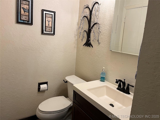 half bathroom featuring a textured wall, vanity, and toilet