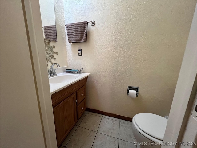 bathroom with a textured wall, tile patterned flooring, toilet, vanity, and baseboards