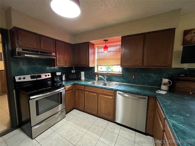 kitchen featuring a textured ceiling, under cabinet range hood, stainless steel appliances, a sink, and dark countertops