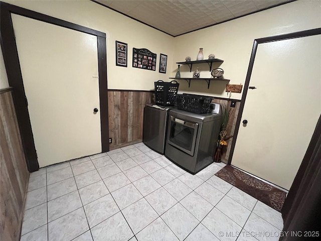 washroom with a wainscoted wall, washing machine and clothes dryer, light tile patterned flooring, wood walls, and laundry area