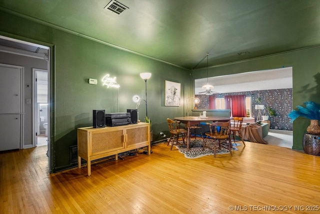 dining area with wallpapered walls, crown molding, visible vents, and hardwood / wood-style floors