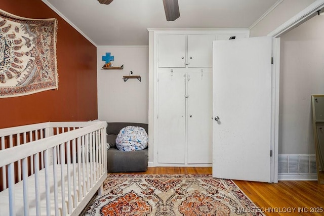 bedroom with ceiling fan, wood finished floors, ornamental molding, a closet, and a crib