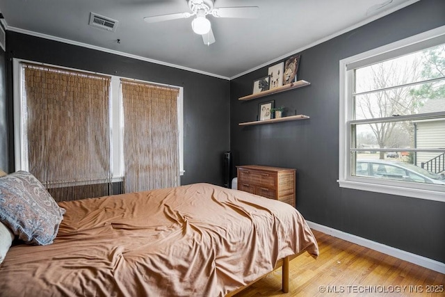 bedroom with multiple windows, wood finished floors, visible vents, and crown molding