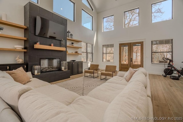 living area with a healthy amount of sunlight, light wood-style floors, french doors, and a tile fireplace