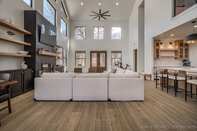 living room featuring light wood-style flooring, recessed lighting, a fireplace, a ceiling fan, and french doors