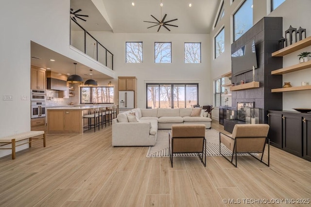 living room featuring ceiling fan, light wood finished floors, and a tiled fireplace